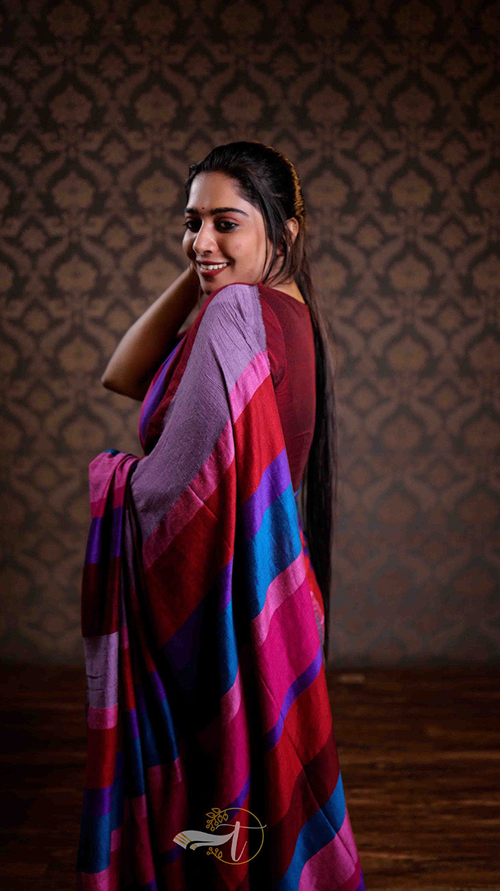 Woman wearing a colorful saree against a patterned wall.