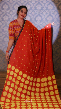Woman wearing a red and yellow saree with a blue patterned wall in the background