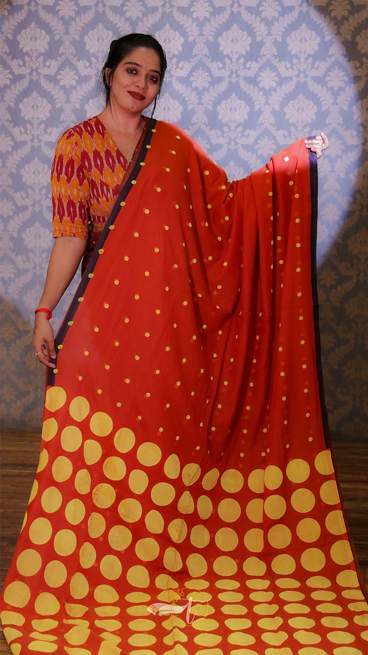 Woman wearing a red and yellow saree with a blue patterned wall in the background