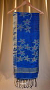 Blue floral-patterned scarf with fringe on a wooden hanger against a beige curtain background