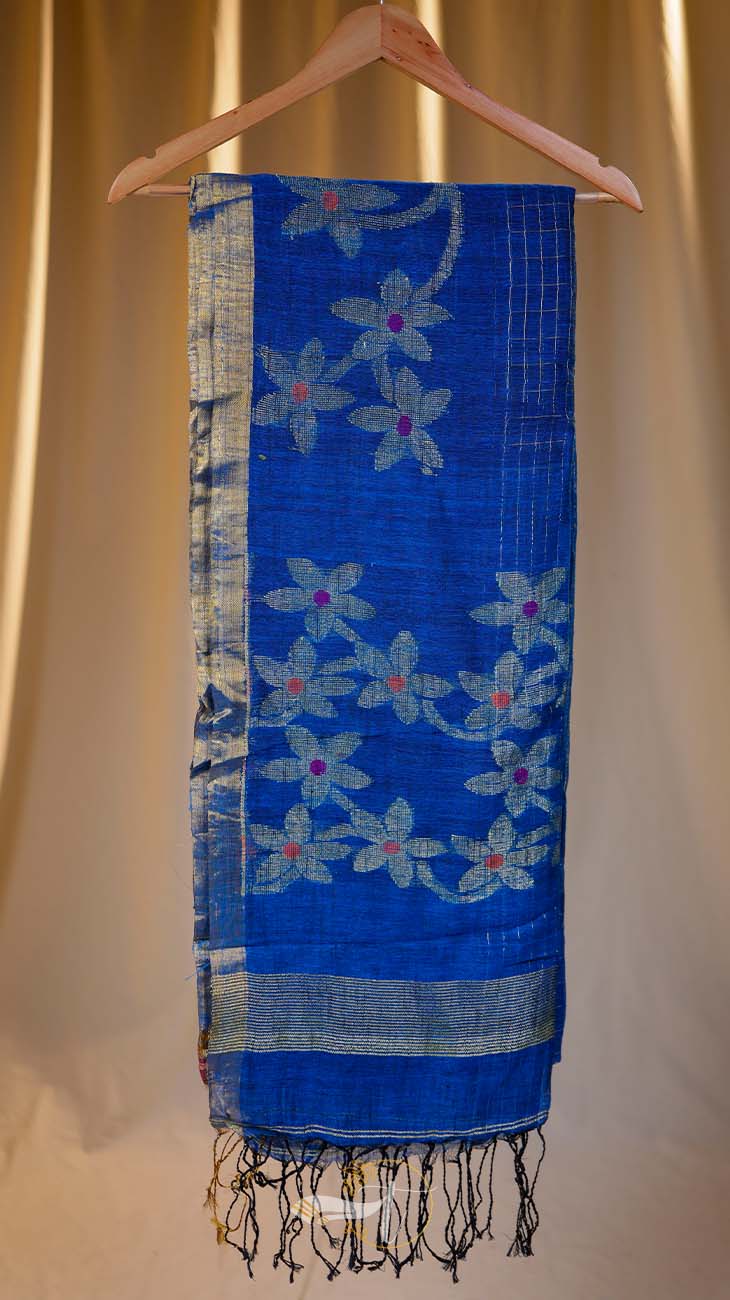 Blue floral-patterned scarf with fringe on a wooden hanger against a beige curtain background