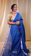 Woman wearing a blue saree with a gold blouse against a beige curtain background