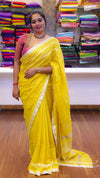Woman in a yellow saree standing in front of a colorful fabric display.
