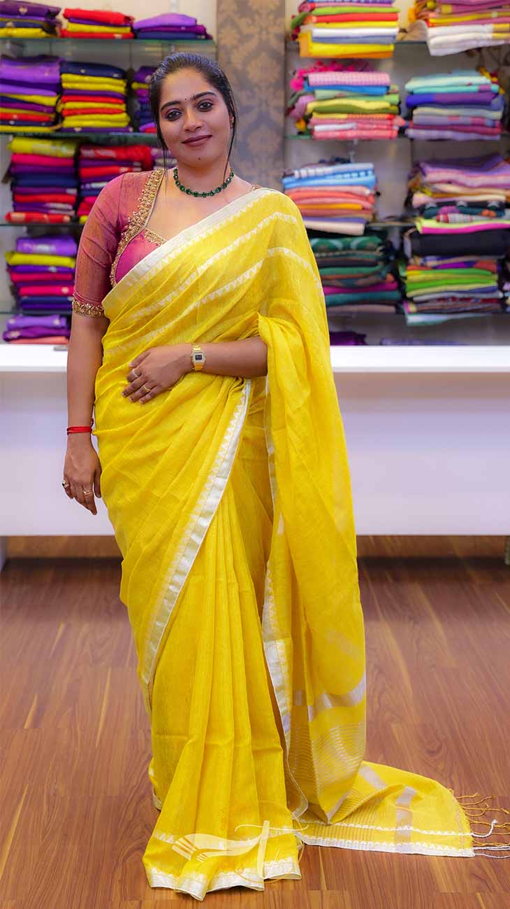 Woman in a yellow saree standing in front of a colorful fabric display.