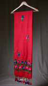 Red scarf with floral embroidery and tassels on a wooden hanger against a neutral background