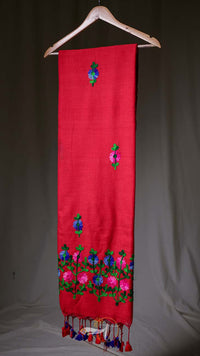 Red scarf with floral embroidery and tassels on a wooden hanger against a neutral background