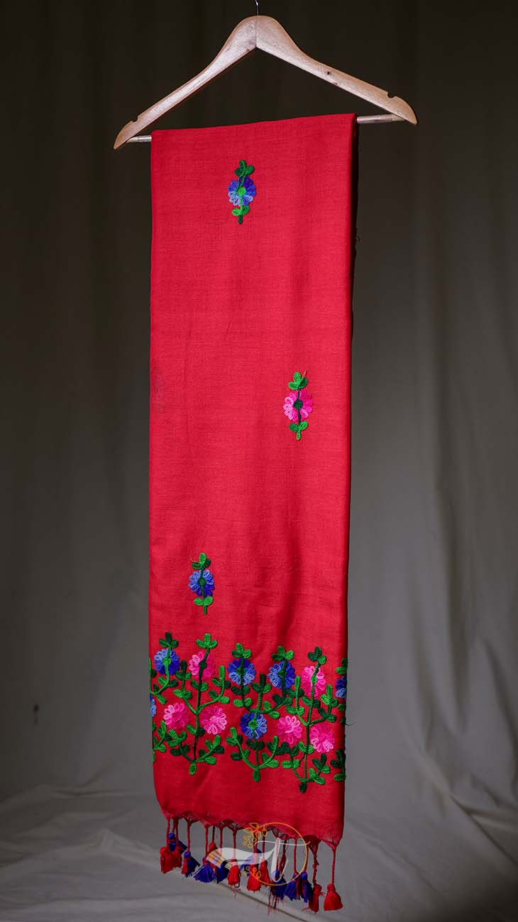 Red scarf with floral embroidery and tassels on a wooden hanger against a neutral background