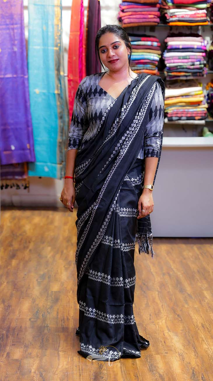 Woman wearing a black saree with a pattern in a fabric store.