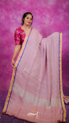 Woman wearing a pink saree with a yellow border against a pink background