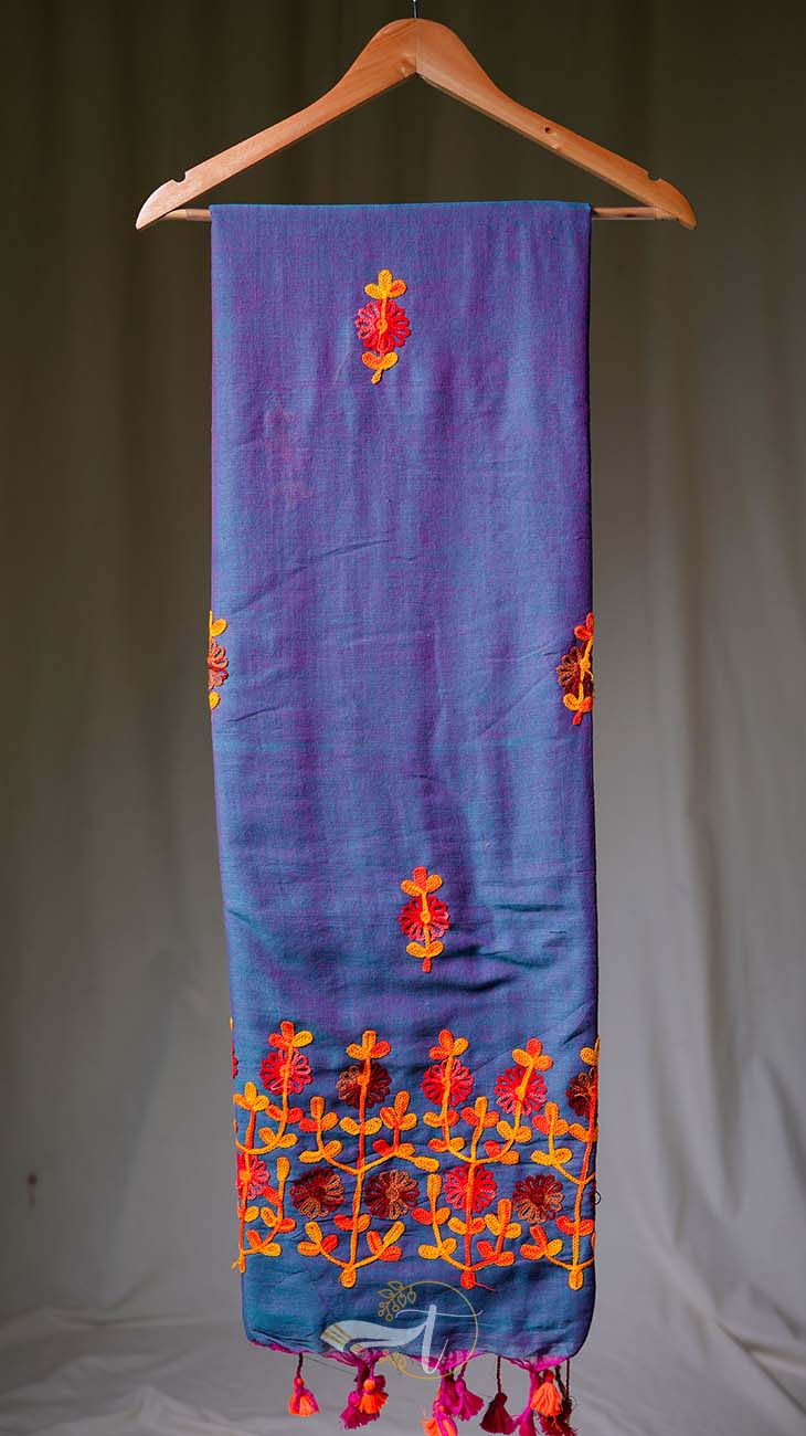 Blue embroidered fabric with orange and red patterns on a hanger against a neutral background