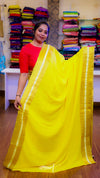 Woman holding a yellow saree with a colorful background of folded fabrics.