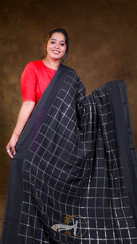 Woman holding a black saree with white patterns against a brown background