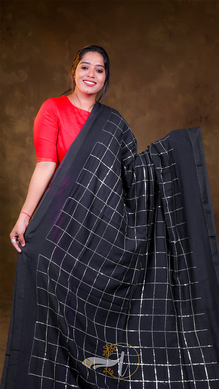 Woman holding a black saree with white patterns against a brown background