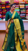Woman wearing a green and yellow saree in front of a colorful fabric display.