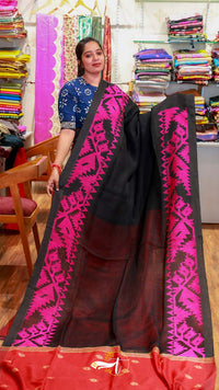 Woman holding a black and pink saree with a fabric store in the background