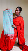 Woman in a red saree holding a light blue checkered fabric against a plain background