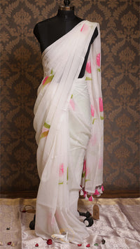 White saree with floral patterns on a mannequin against a patterned wall.