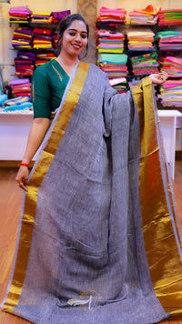 Woman holding a gray saree with a gold border in a fabric store.