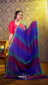 Woman holding a colorful striped saree against a patterned wall.