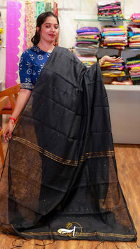Woman holding a black saree with a blurred background of fabric stacks