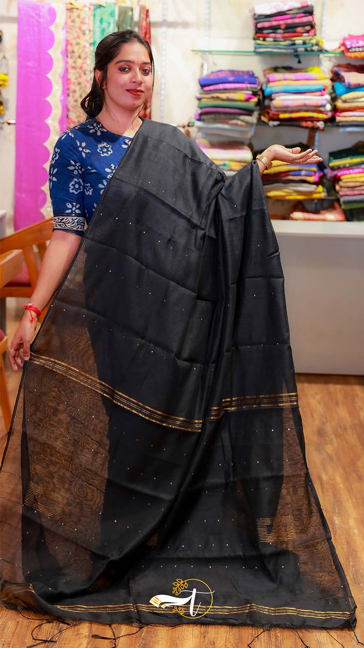 Woman holding a black saree with a blurred background of fabric stacks
