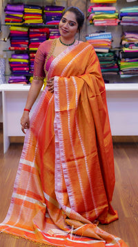 Woman wearing an orange saree with a white border in a store setting.