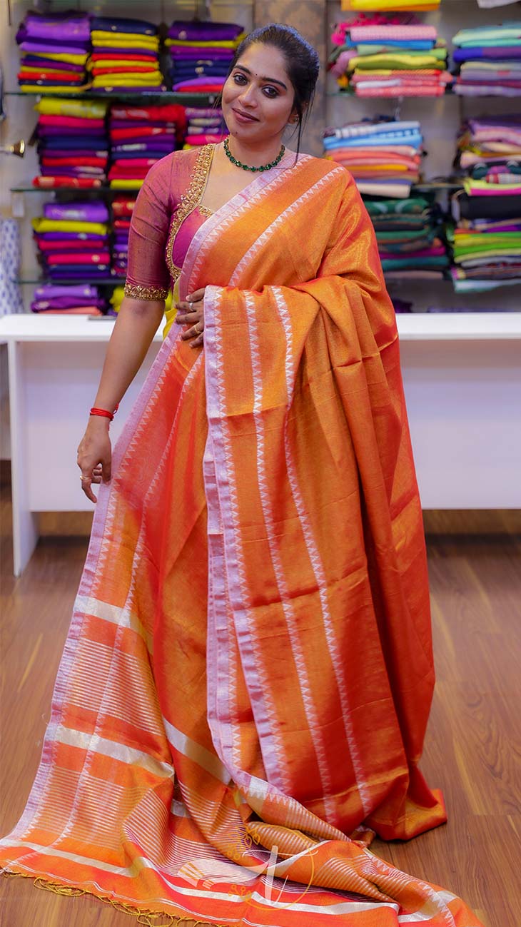 Woman wearing an orange saree with a white border in a store setting.