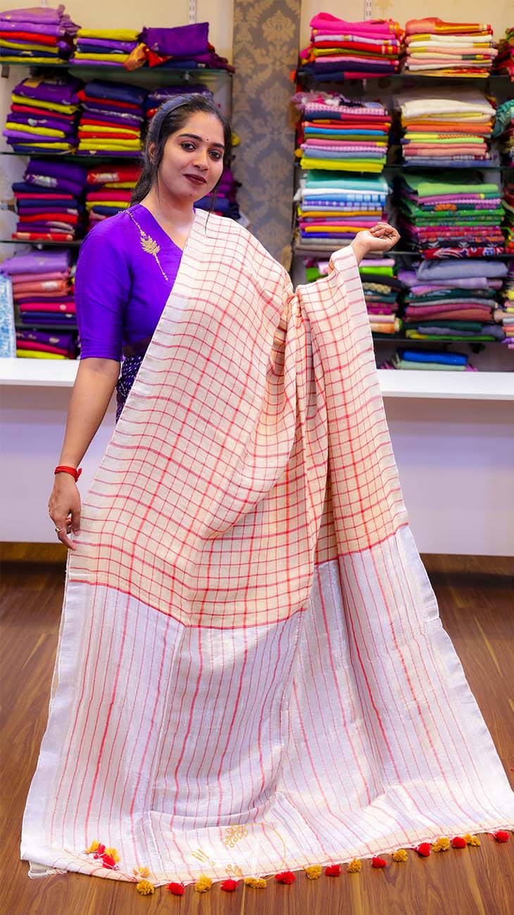 Woman holding a white saree with red and orange stripes in a fabric store.