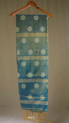 Blue fabric with white polka dots and gold accents hanging on a wooden hanger against a beige background.