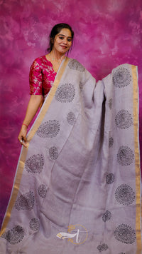 Woman wearing a white saree with black patterns against a pink background