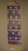 Purple scarf with white polka dots and gold fringe on a hanger against a beige background