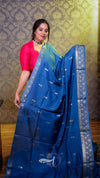 Woman holding a blue saree with a pattern against a decorative wall.