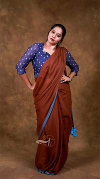 Woman wearing a brown saree with a blue blouse against a brown background