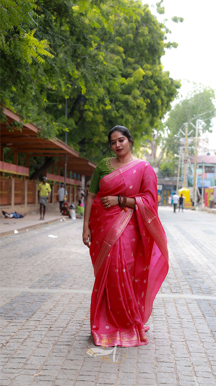 Woman in a pink saree standing on a street with greenery in the background