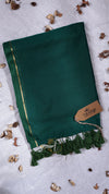 Green scarf with gold trim and a tag on a light gray background with dried leaves.