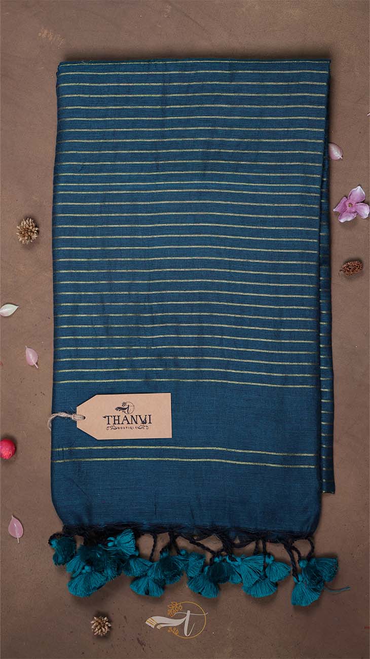 Blue striped towel with tassels on a brown background, featuring a 'THANU' tag.