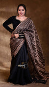 Woman wearing a black saree with a gold border against a brown background