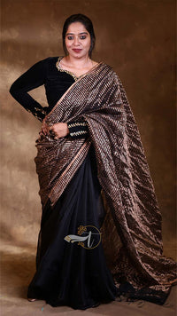 Woman wearing a black saree with a gold border against a brown background