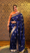 Woman wearing a blue saree with a pattern against a decorative wall.