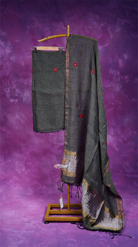 Dark gray saree with red buttons and gold patterns on a wooden stand against a purple background