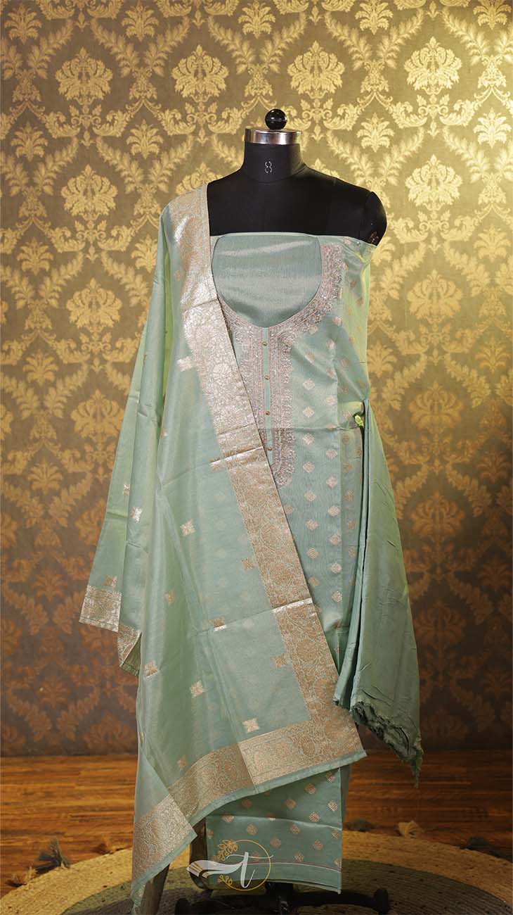 Light green traditional outfit with embroidery on a mannequin against a patterned wall.