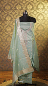 Light green traditional outfit with embroidery on a mannequin against a patterned wall.
