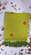 Green scarf with red hearts and tassels on a textured surface with dried leaves.