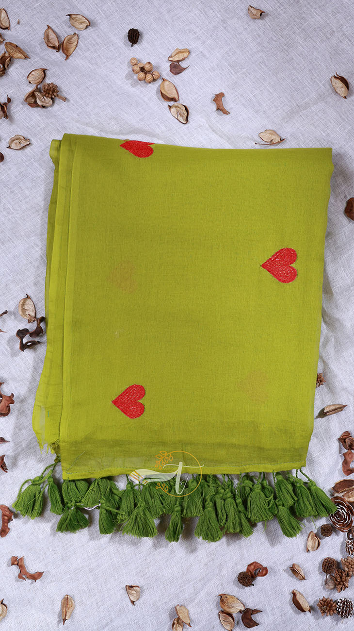 Green scarf with red hearts and tassels on a textured surface with dried leaves.