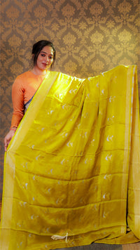 Woman holding a yellow saree with a pattern against a decorative wall.
