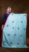 Woman holding a large light blue saree with black patterns against a brown background