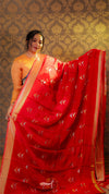 Woman wearing a red saree with a gold border against a patterned wall.