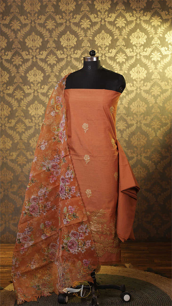 Orange saree with floral patterns on a mannequin against a patterned wall.