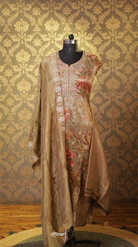 Mannequin wearing a beige embroidered dress against a patterned wall.