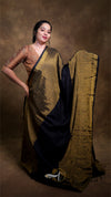 Woman wearing a traditional saree with a gold and black pattern against a brown background